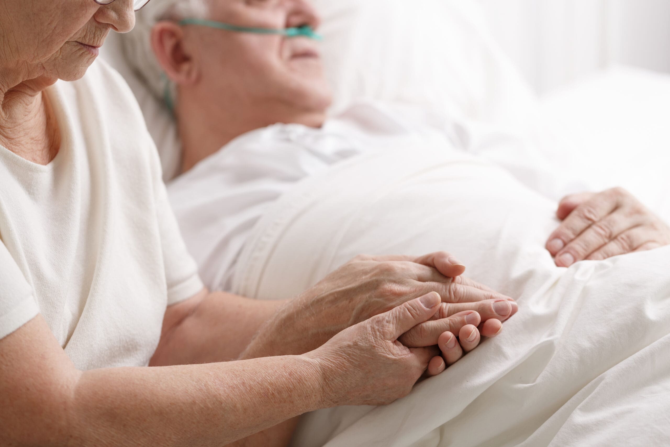 Elderly woman holding hand of husband who is on oxygen